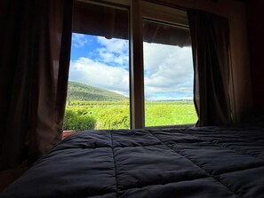 En seng med udsigt til et grønt landskab gennem et vindue.