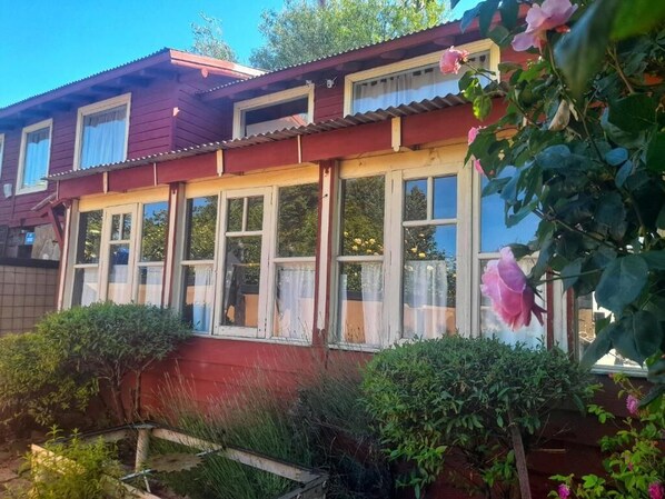 Una casa de dos pisos con fachada roja, varias ventanas y un jardín con diversas plantas y flores.