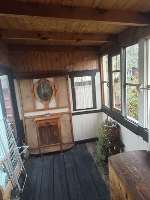 Un interior de madera con techo de madera, una ventana con cortinas blancas, un armario de madera y una reja de metal.