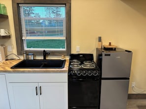 Een keuken met een zwarte kookplaat, een koelkast, een raam met zonwering en een spoelbak.