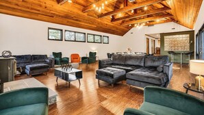 Amplia sala de estar con techo de madera alto, diversas opciones de asiento que incluyen sofás y sillones, y ventanas grandes que dejan entrar luz natural.