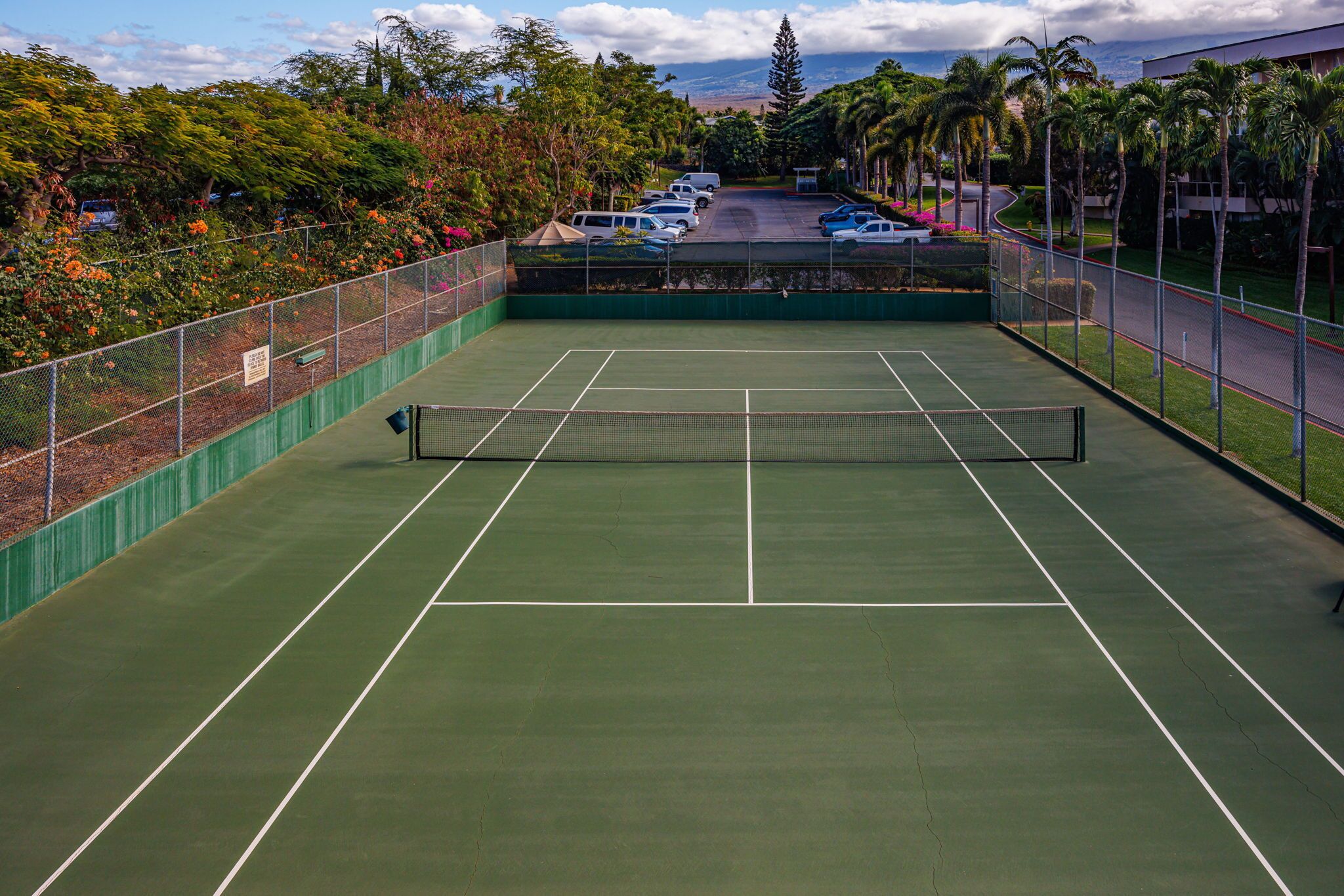 A tennis court with a net, surrounded by a fence and trees.