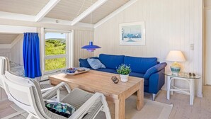Ein Zimmer mit einem Holztisch, einem blauen Sofa, weißen Stühlen, einem Glastisch und einer Lampe.