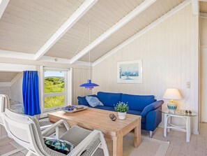 Ein Zimmer mit einem Holztisch, einem blauen Sofa, weißen Stühlen, einem Glastisch und einer Lampe.
