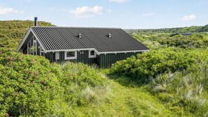 Ein modernes Haus mit geneigtem Dach, umgeben von üppiger Vegetation und Hügeln.