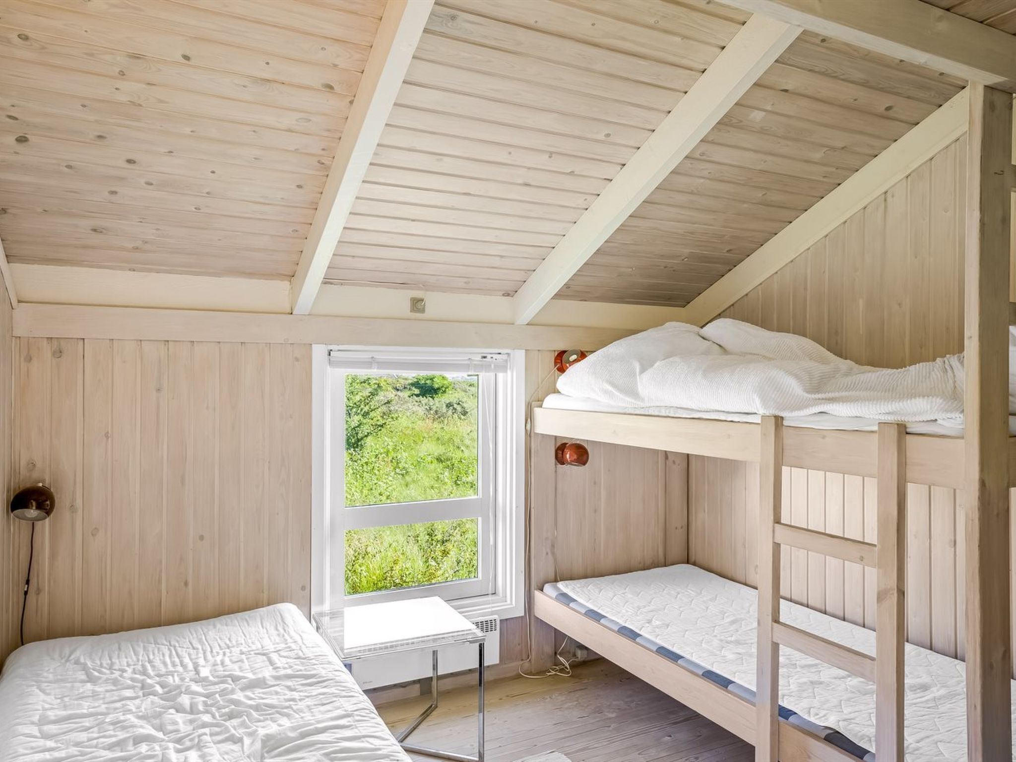 Een slaapkamer met stapelbed, raam, nachtkastje en lamp.