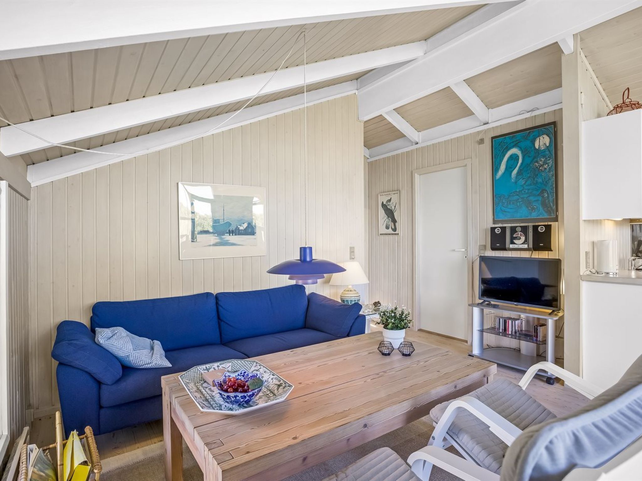 A room with a blue sofa, a wooden coffee table, a lamp, and a painting on the wall.