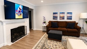 Ein Wohnzimmer mit Kamin, braunem Sofa, Fernseher und einem gemusterten Teppich.