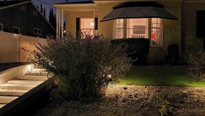 Ein Haus mit einer gut beleuchteten Einfahrt, einer Treppe zum Eingang und einem kleinen Garten.