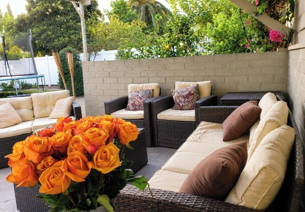 An outdoor seating area with wicker furniture, a brick wall, and a variety of plants. - Urban Oasis: Private 2BR + Lush Backyard in LA (Los Angeles)