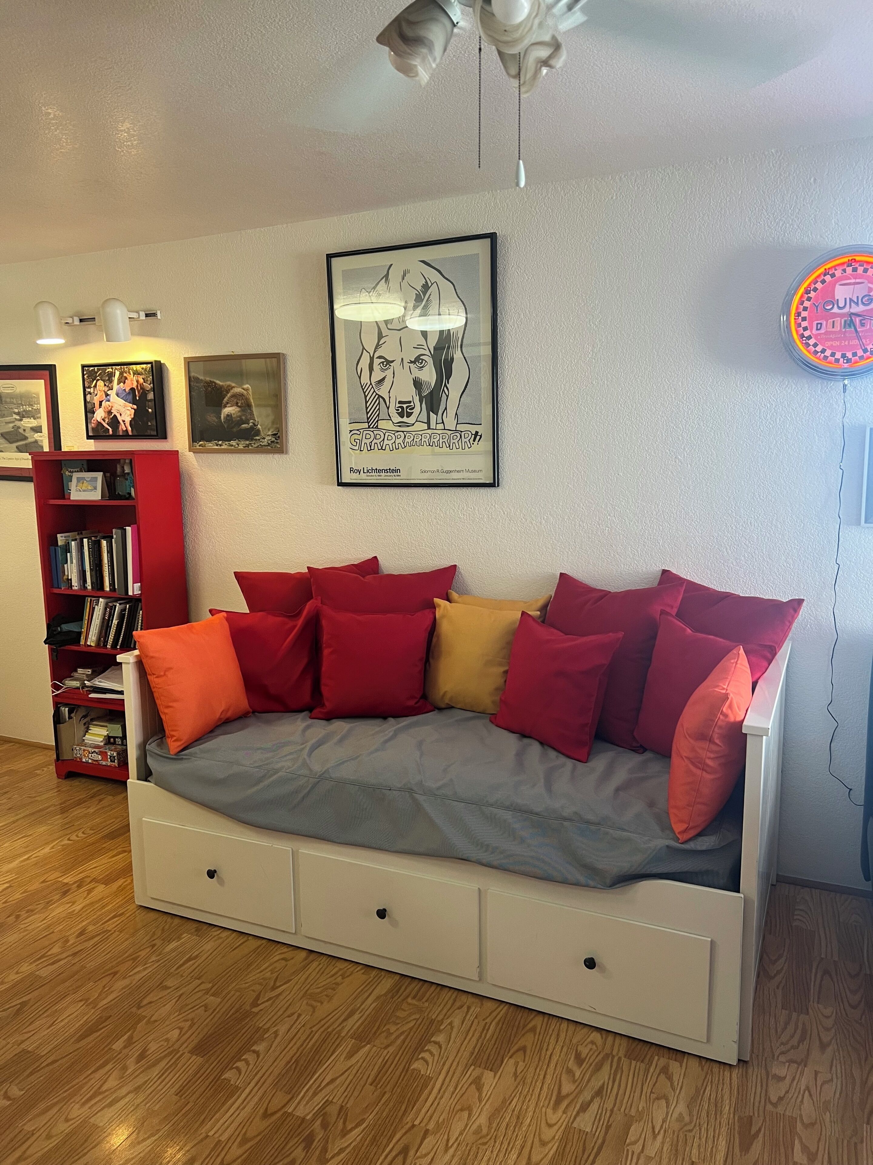 Une chambre à coucher avec un lit, une bibliothèque, un tableau encadré et un ventilateur de plafond.