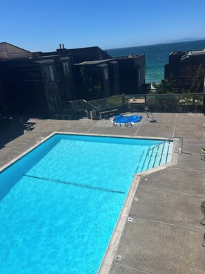 A swimming pool with clear blue water, surrounded by a stone deck, and overlooking a body of water.