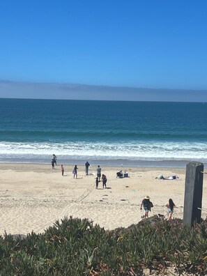 A beach with people, a wooden post, and a clear sky.