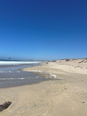 A beach with clear skies, calm waters, and a few people walking.
