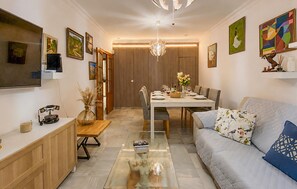Ein modernes Wohnzimmer mit Essbereich, ausgestattet mit einer Couch, einem Couchtisch, einem Esstisch für vier Personen und einer dekorativen Skulptur.