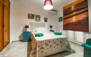 Ein Schlafzimmer mit einem Bett, zwei Nachttischen, einem Fenster mit Jalousien und einer Wand-Klimaanlage.