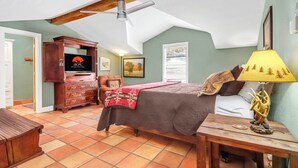 Ein Schlafzimmer mit einem Bett, einer Holzkommode, einem Deckenventilator, einer Lampe und einem Fenster mit Jalousien.