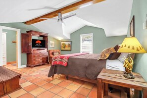 Ein Schlafzimmer mit einem Bett, einer Holzkommode, einem Deckenventilator, einer Lampe und einem Fenster mit Jalousien.