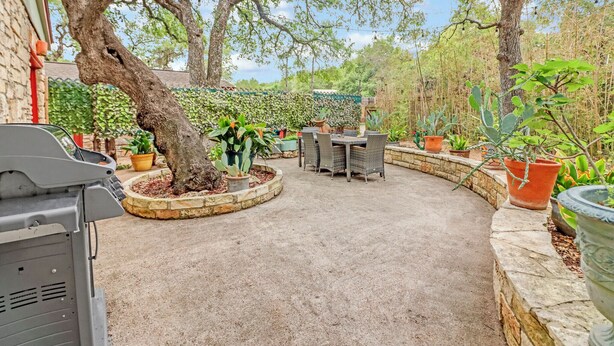 Eine Terrasse mit Grill, Gartenmöbeln und Topfpflanzen.