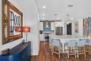 Una cocina moderna con armarios blancos, una isla central con taburetes altos, una lámpara roja y una obra de arte enmarcada en la pared.