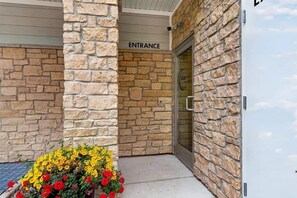 Entrada a un edificio de piedra con un letrero que dice 'ENTRANCE' y un cantero con flores amarillas y rojas.