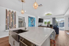 A modern kitchen with a large island, pendant lights, and a view to the outside.