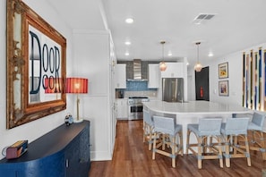 A modern kitchen with white cabinets, a central island with bar stools, a red lamp, and a framed artwork on the wall.
