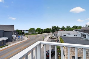 Straßenansicht mit einem Gebäude links, blauem Himmel und Bäumen im Hintergrund.