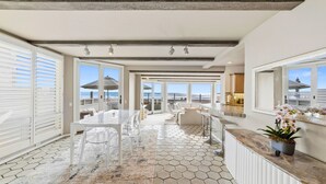 A spacious balcony with a view of the ocean, a dining area with a glass table, and a kitchen area.