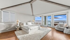 A bedroom with a large bed, a sofa, a glass table, and a view of the ocean.