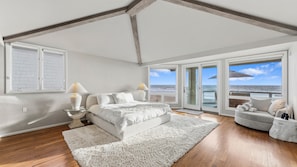 Ein Schlafzimmer mit einem großen Bett, einem Sofa, einem Glastisch und Blick auf den Ozean.