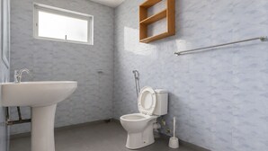 Une salle de bain avec des toilettes, un lavabo, une fenêtre et une étagère en bois.