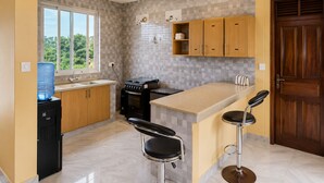 Une cuisine compacte équipée d’un distributeur d’eau, d’une cuisinière et de deux tabourets de bar.