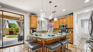 A modern kitchen with a central island, bar stools, pendant lights, and wooden cabinets. - 4BR w putting green, gym, outdoor kitchen (Queen Creek)