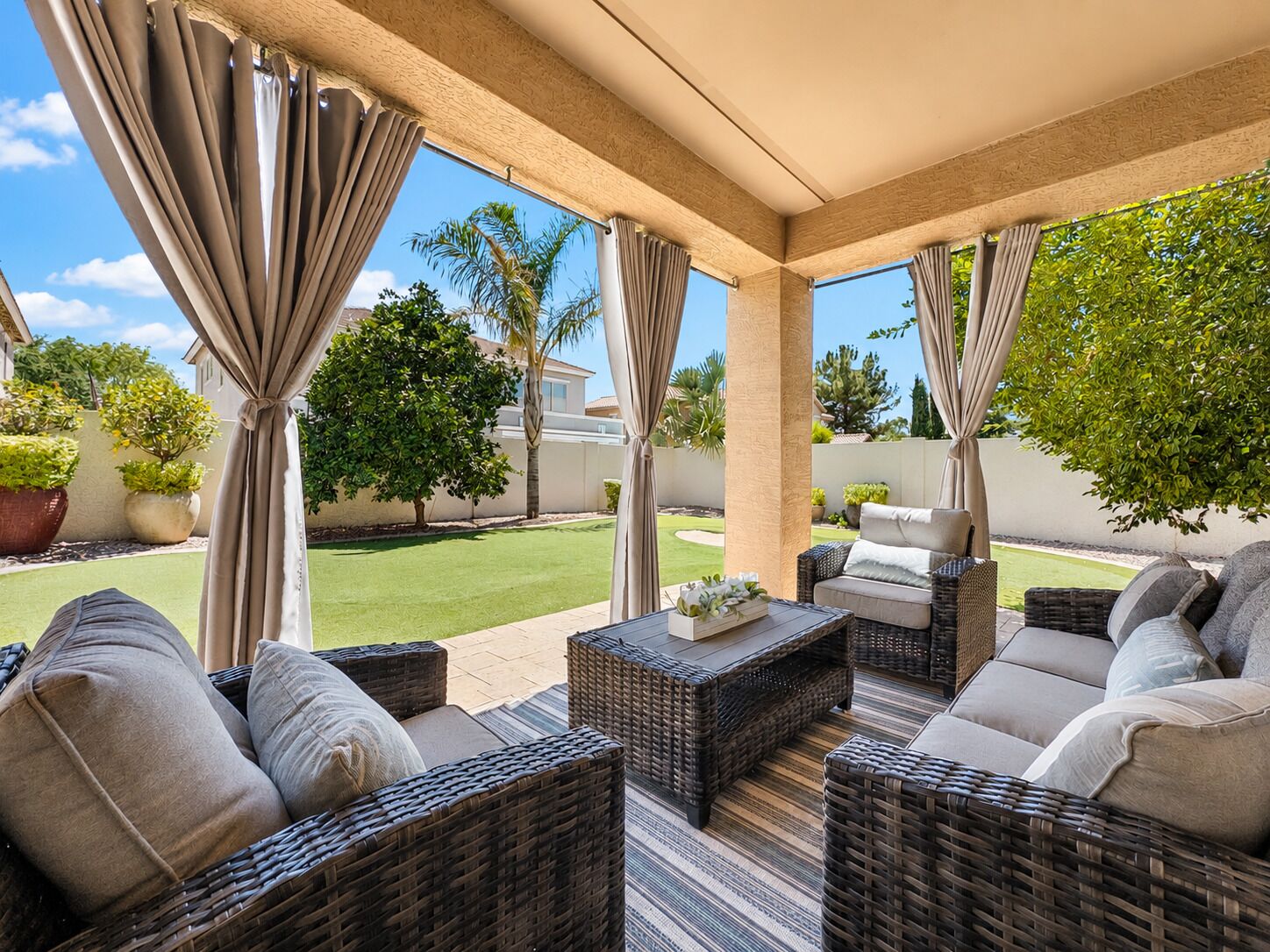 Une terrasse couverte, aménagée avec des meubles en osier, et offrant une vue sur une pelouse bien entretenue et des arbres.