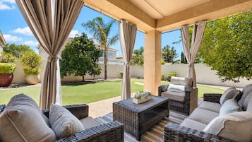 Une terrasse couverte, aménagée avec des meubles en osier, et offrant une vue sur une pelouse bien entretenue et des arbres.