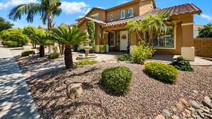 A two-story house with a tiled roof, a front porch, and a landscaped garden with palm trees and shrubs. - 4BR w putting green, gym, outdoor kitchen (Queen Creek)