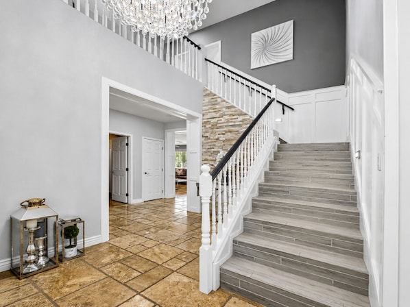 Eine Treppe mit weißen Balustraden und Holzvertäfelung, die zu einer Empore mit einem Chandelier führt.