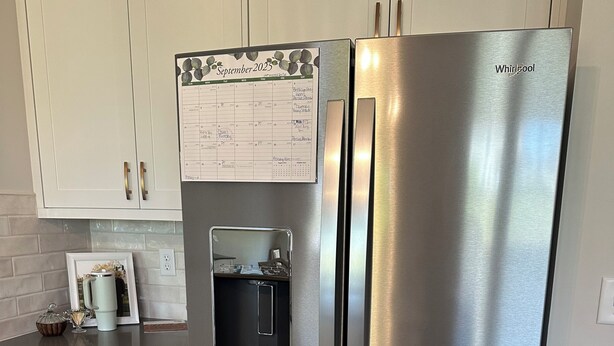 Ein Edelstahl-Kühlschrank von Whirlpool mit Wasserspender, einem Kalender und einem gerahmten Bild auf der Arbeitsfläche.