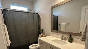 Ein Badezimmer mit Toilette, Waschbecken, Spiegel, Duschvorhang und gemusterten Teppichen.