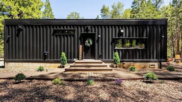 Un bâtiment moderne de couleur noire, doté d’une terrasse en bois, d’une pancarte d’accueil et de petites plantes en pot.