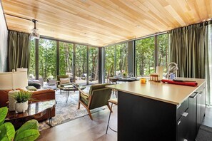 Una cocina moderna con una isla grande, comedor con sillas y vistas al bosque a través de amplios ventanales.