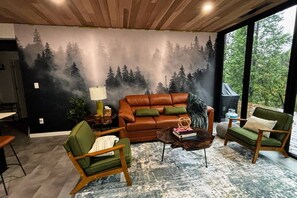 Un salon avec une fresque représentant une forêt, un canapé en cuir marron, des fauteuils verts et une table basse.