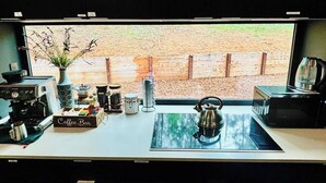 Een keuken met een koffiebar, een waterkoker en uitzicht op een houten schutting.