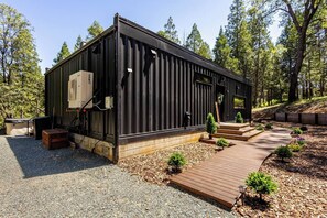 En modern stuga med en träveranda, en liten sittplats utomhus och en gångstig som leder till entrén.
