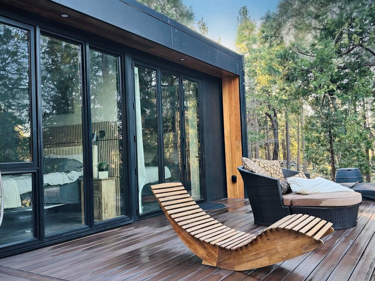 Eine Terrasse mit Liegestuhl aus Holz und einer gepolsterten Sitzecke, großen Glasfenstern und einer Holzterrasse.
