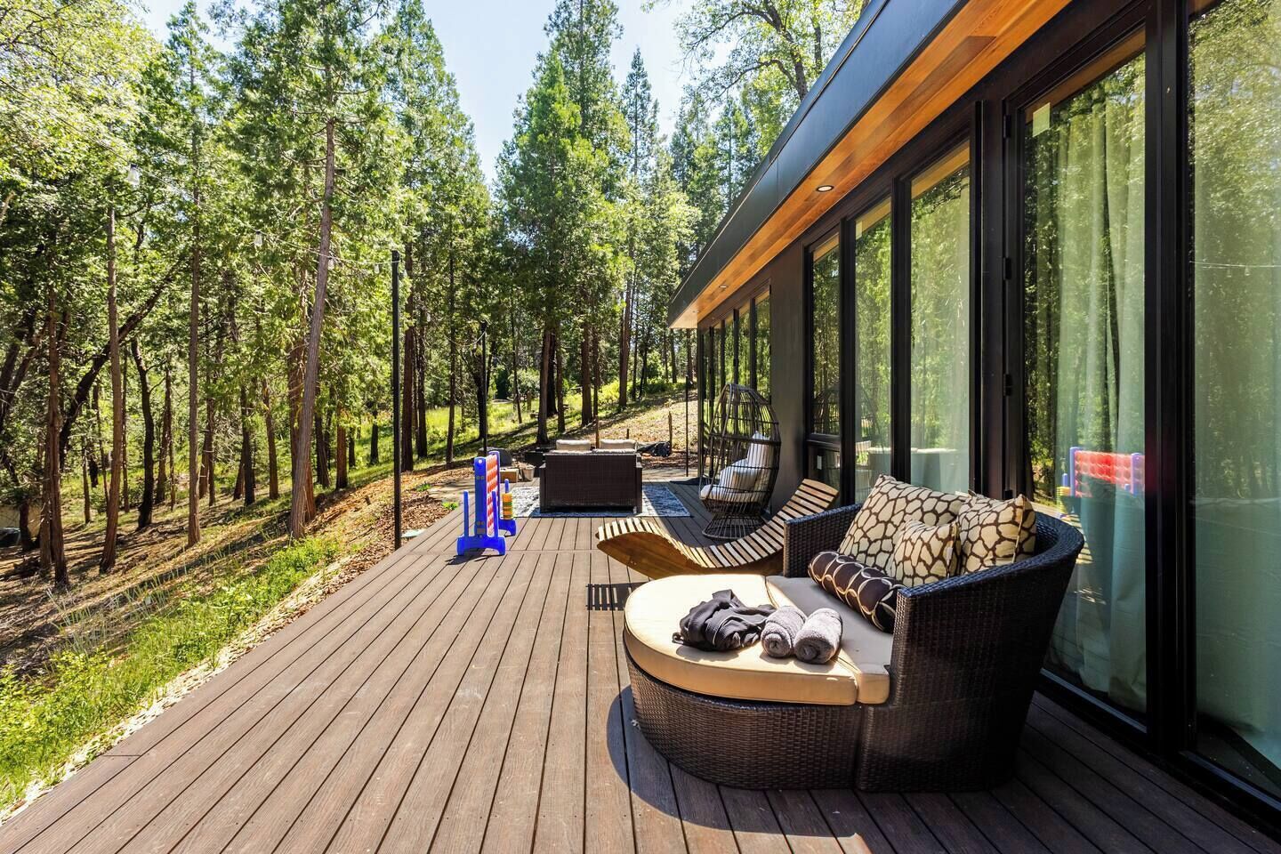 En terrasse med udendørs møbler, pejse og en glasvæg med udsigt til en skov.