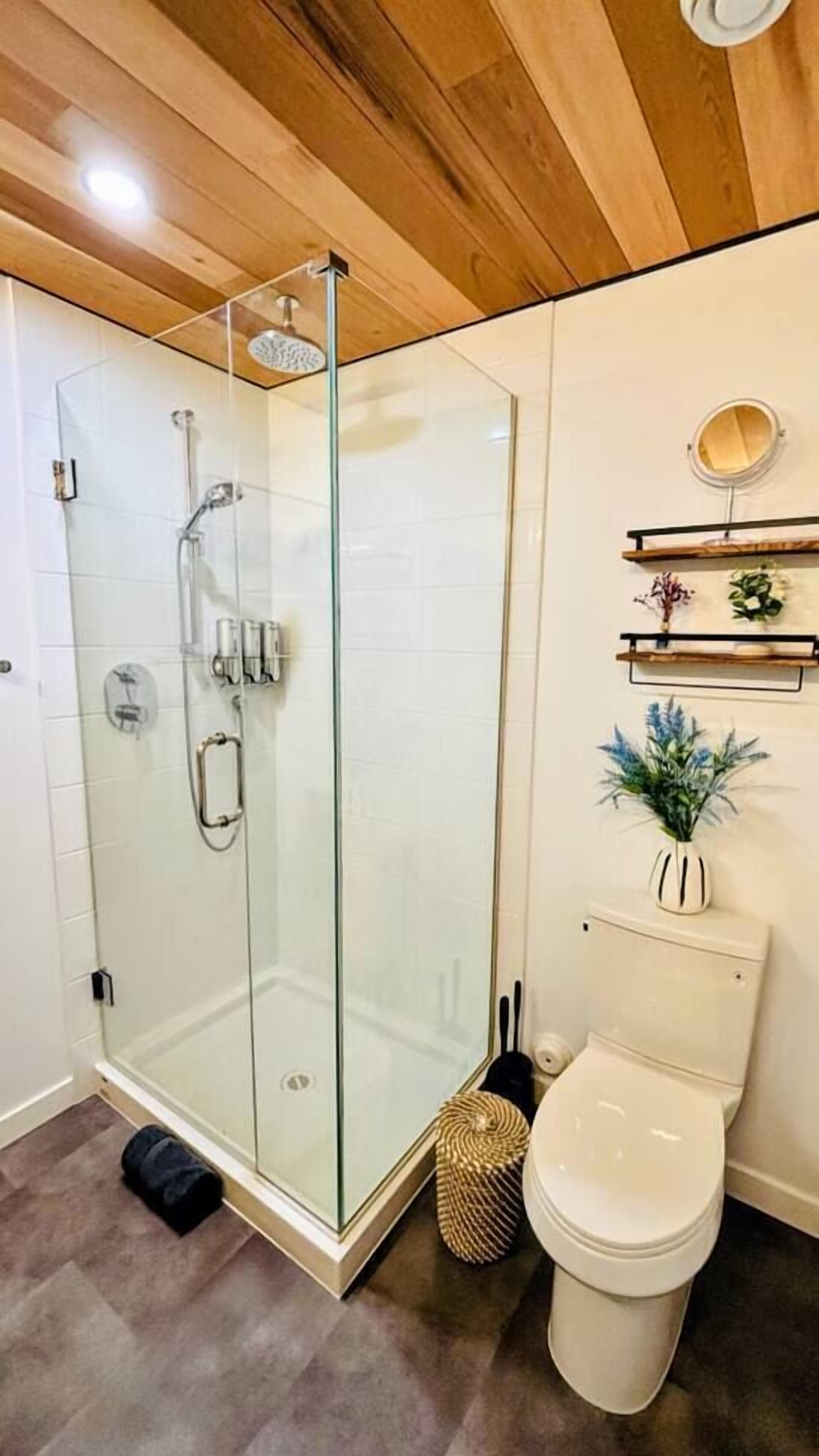 Et moderne badeværelse med et glasafskærmet brusebad, toilet og en lille hylde med dekorative genstande.