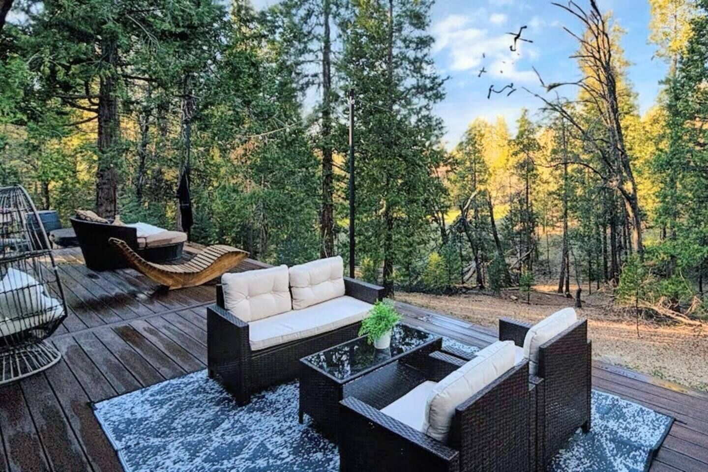 A deck with outdoor furniture, including a sofa and chairs, surrounded by a forest.