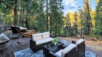A deck with outdoor furniture, including a sofa and chairs, surrounded by a forest.